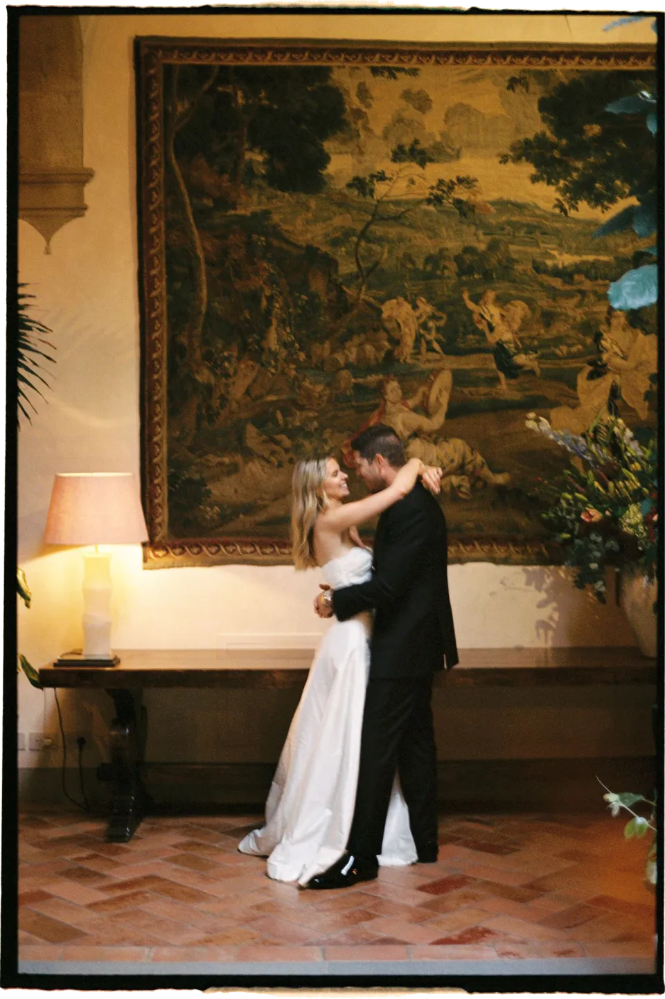 Holly and Matthew dancing together beneath a tapestry in the villa interior, at Villa San Michele in Fiesole above Florence, Tuscany, Italy, for an Elopement Collective elopement. Film photograph by Khara from House of Lucie.