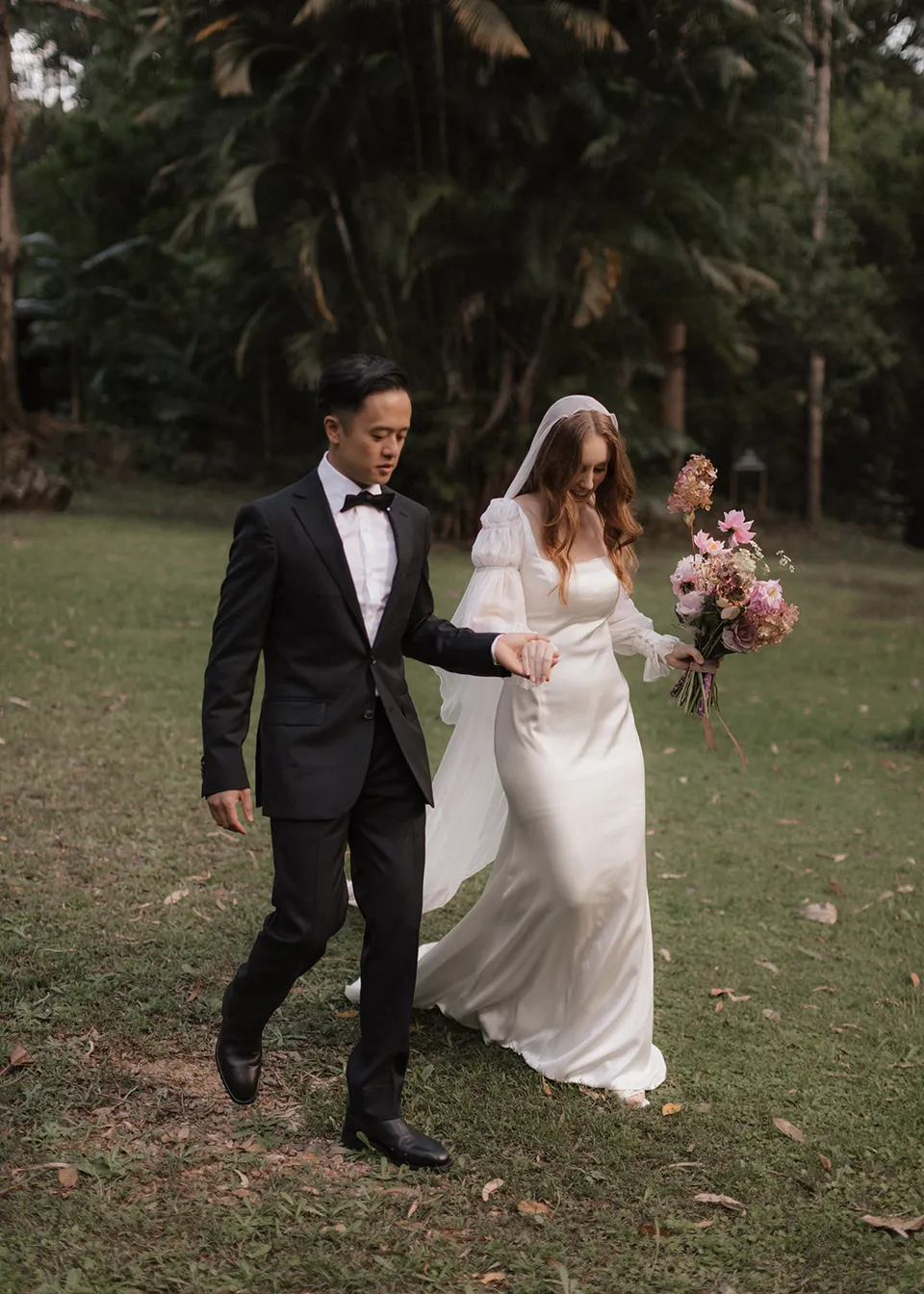 Elyse and Jonathan walking hand in hand across the lawn. At Fig Tree Villa in Ewingsdale, Byron Bay, for an Elopement Collective elopement. Photograph by Bulb Creative.