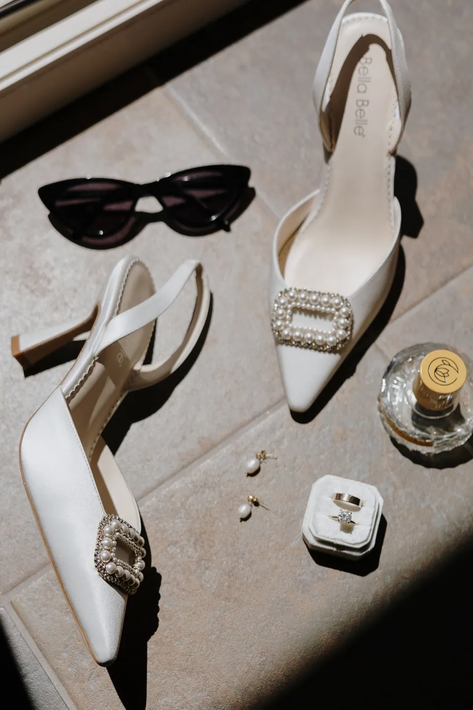 Cream pointed heels with jewelled buckles, sunglasses, rings, jewellery and perfume arranged on a chair at Hotel Villa Marie in Tremezzo, at Lake Como in Lombardy, Italy, for an Elopement Collective elopement. Photograph by George Bowden.