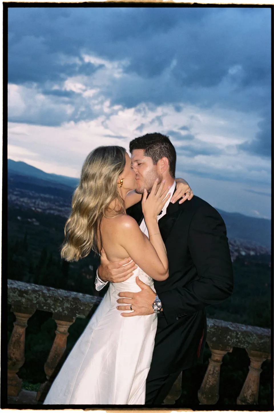 Holly and Matthew kissing close together with dark clouds above the Florence skyline, at Villa San Michele in Fiesole above Florence, Tuscany, Italy, for an Elopement Collective elopement. Film photograph by Khara from House of Lucie.