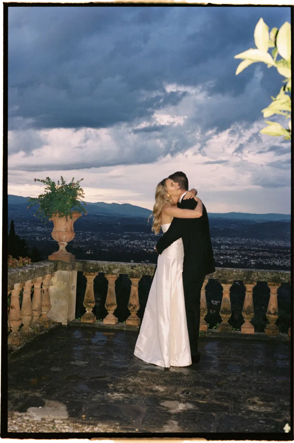 Holly and Matthew embracing on the terrace, lit by flash beneath gathering clouds, at Villa San Michele in Fiesole above Florence, Tuscany, Italy, for an Elopement Collective elopement. Film photograph by Khara from House of Lucie.