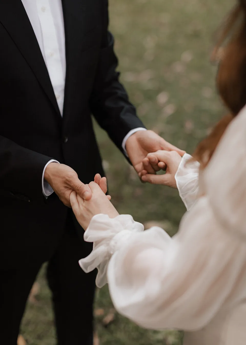 Close-up of Elyse and Jonathan's joined hands beneath her gathered sleeve. At Fig Tree Villa in Ewingsdale, Byron Bay, for an Elopement Collective elopement. Photograph by Bulb Creative.