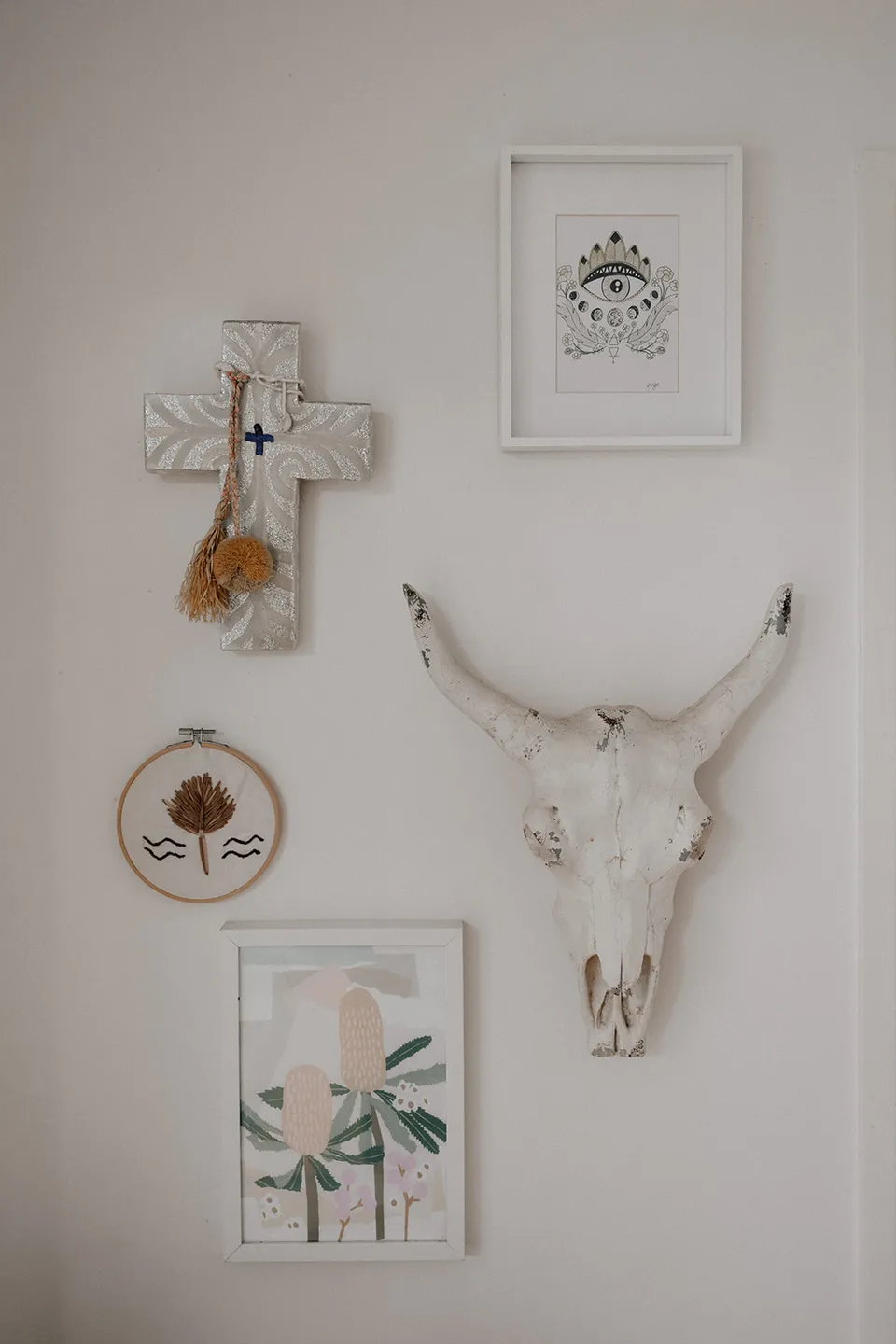 Framed artworks, a cross and a decorative horned skull on a white interior wall, at Grounds of Cabarita in Cabarita Beach, NSW, for an Elopement Collective elopement. Photo by Bulb Creative.