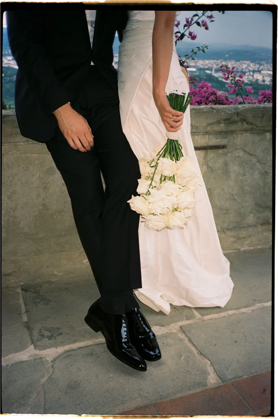 Close view of Holly’s white bouquet by Le Francesche Flower Designers and wedding dress beside Matthew’s black suit, at Villa San Michele in Fiesole above Florence, Tuscany, Italy, for an Elopement Collective elopement. Film photograph by Khara from House of Lucie.