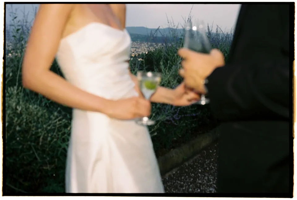Close view of Holly’s white dress and the couple’s wine glasses in the evening light, at Villa San Michele in Fiesole above Florence, Tuscany, Italy, for an Elopement Collective elopement. Film photograph by Khara from House of Lucie.