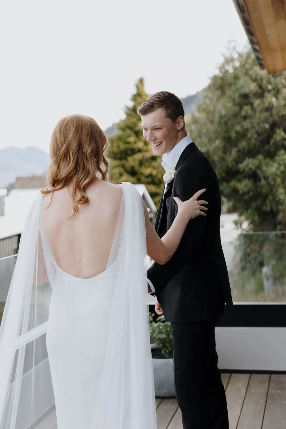 Hamish smiling as he turns to see Neve during their first look on the terrace, at their Airbnb in Fernhill, Queenstown, New Zealand, for an Elopement Collective Queenstown elopement. Photo by George Bowden.