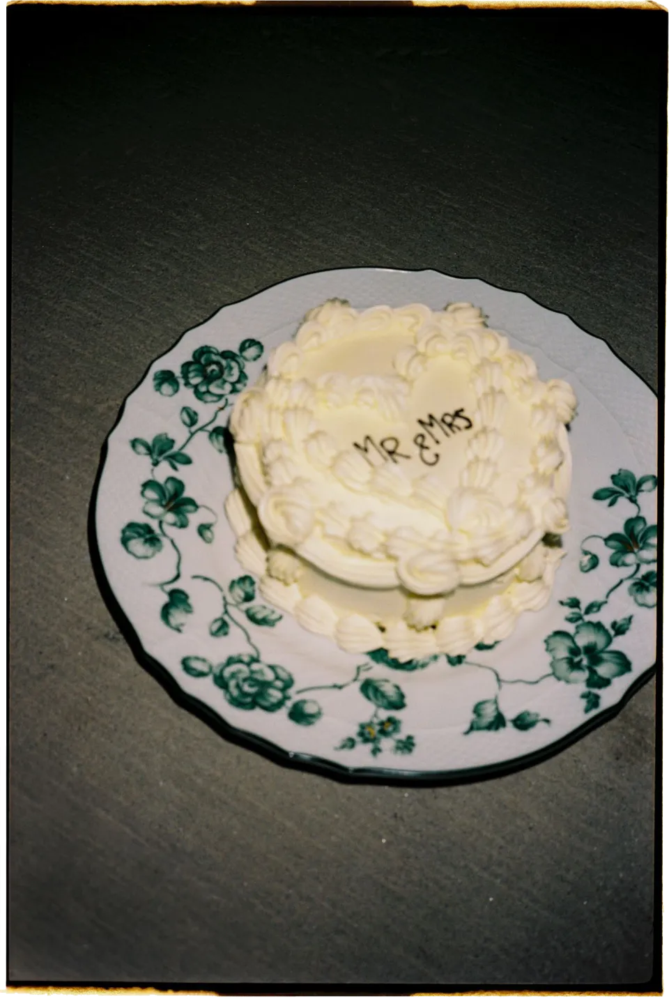 A small white iced wedding cake on a patterned plate, at Villa San Michele in Fiesole above Florence, Tuscany, Italy, for an Elopement Collective elopement. Film photograph by Khara from House of Lucie.