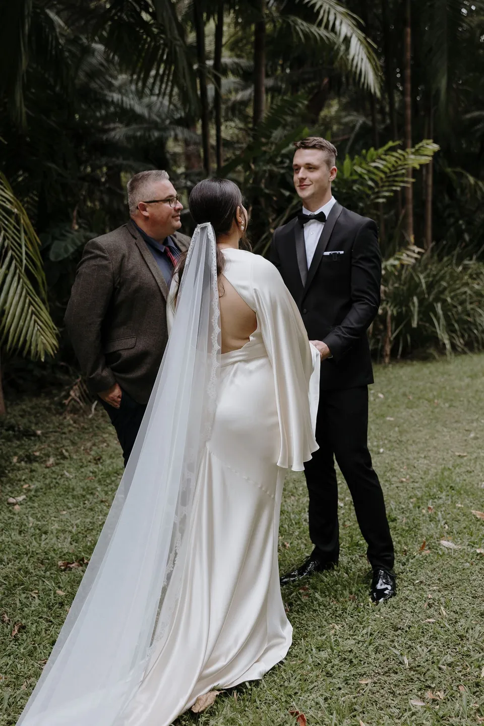 Josh Withers leading Laura and Matthew's ceremony in the palm-filled garden. At Fig Tree Villa in Ewingsdale, Byron Bay, for an Elopement Collective elopement. Photograph by George Bowden.