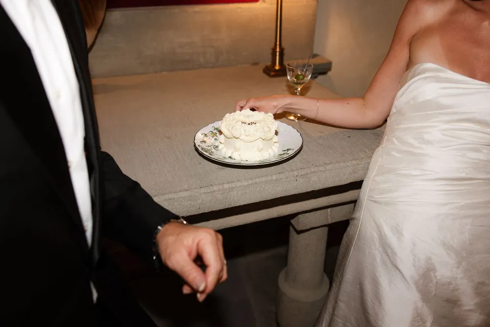 The wedding cake and a glass of wine beside Holly’s white dress and Matthew’s black suit, at Villa San Michele in Fiesole above Florence, Tuscany, Italy, for an Elopement Collective elopement. Digital photograph by Khara from House of Lucie.