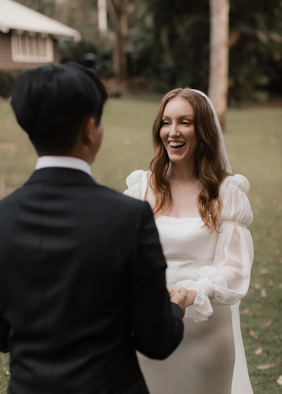 Elyse laughing as she faces Jonathan during their ceremony. At Fig Tree Villa in Ewingsdale, Byron Bay, for an Elopement Collective elopement. Photograph by Bulb Creative.