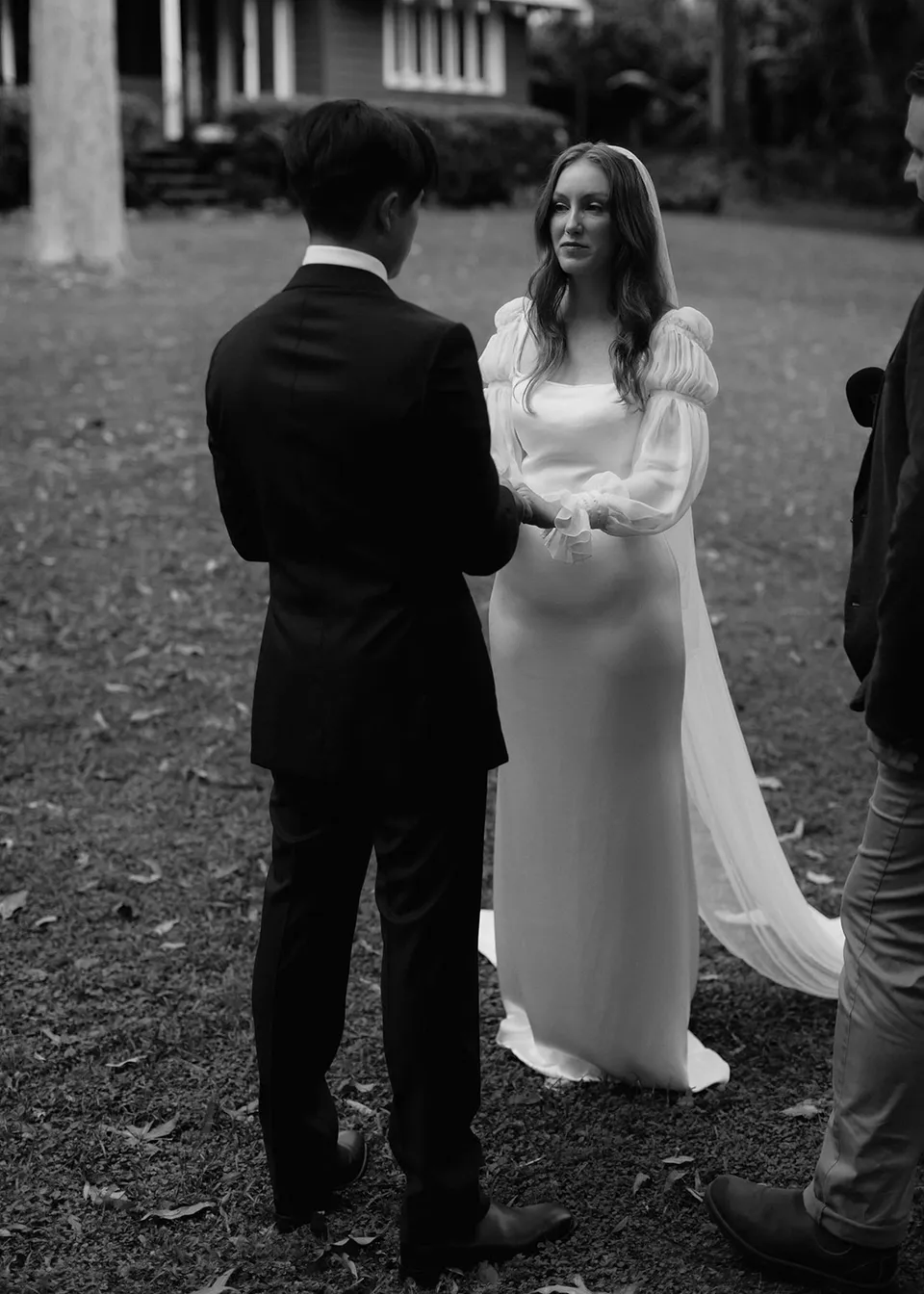 Black-and-white portrait of Elyse smiling at Jonathan while they hold hands. At Fig Tree Villa in Ewingsdale, Byron Bay, for an Elopement Collective elopement. Photograph by Bulb Creative.