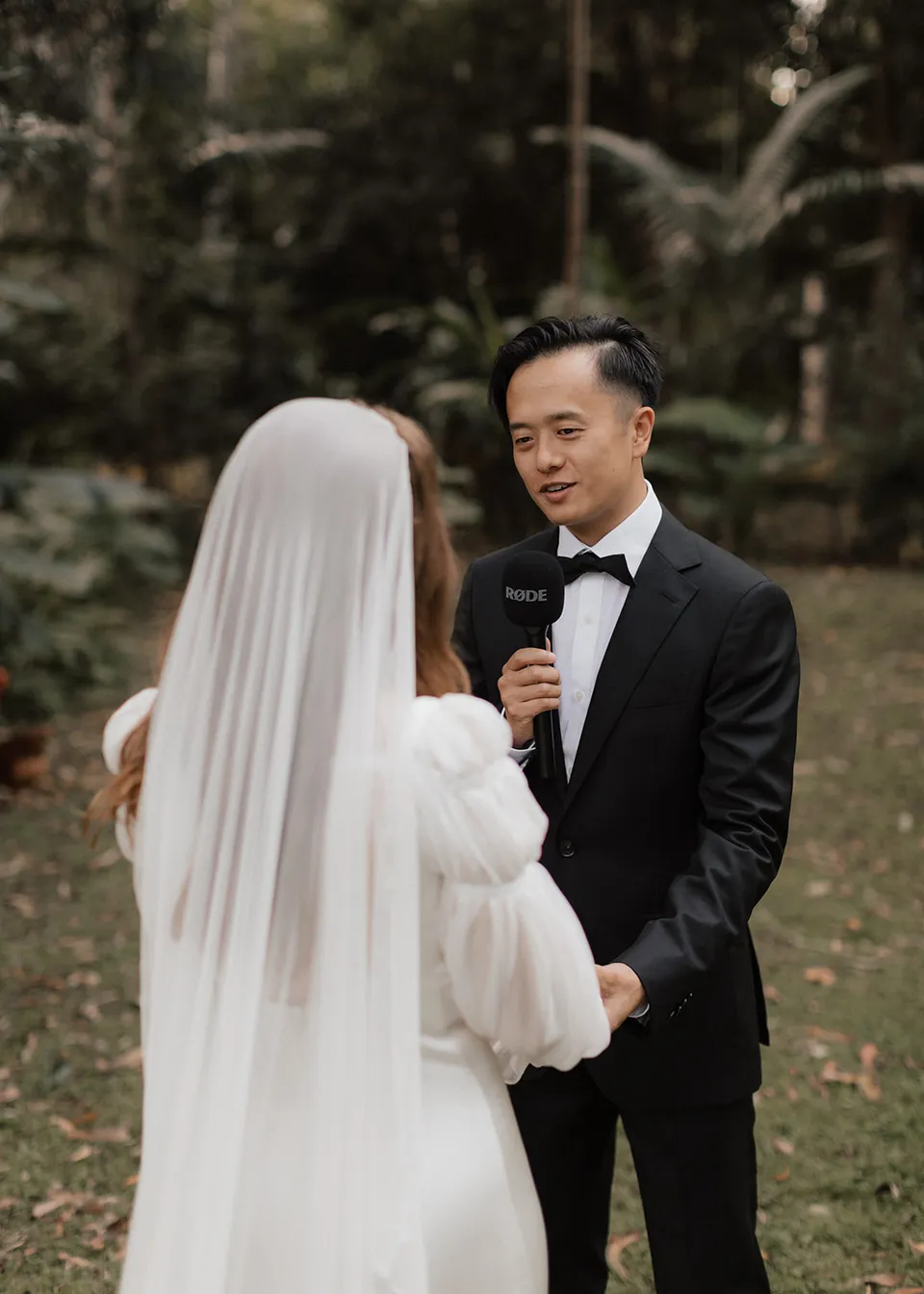 Jonathan speaking his personal vows into a microphone. At Fig Tree Villa in Ewingsdale, Byron Bay, for an Elopement Collective elopement. Photograph by Bulb Creative.