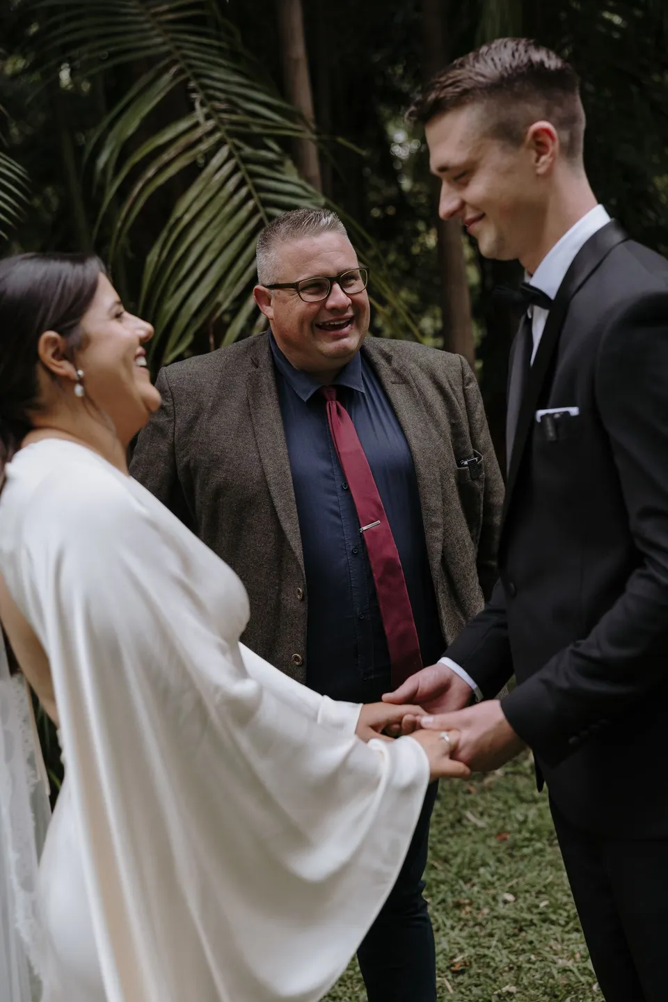 Laura and Matthew laughing with Josh Withers during their ceremony. At Fig Tree Villa in Ewingsdale, Byron Bay, for an Elopement Collective elopement. Photograph by George Bowden.