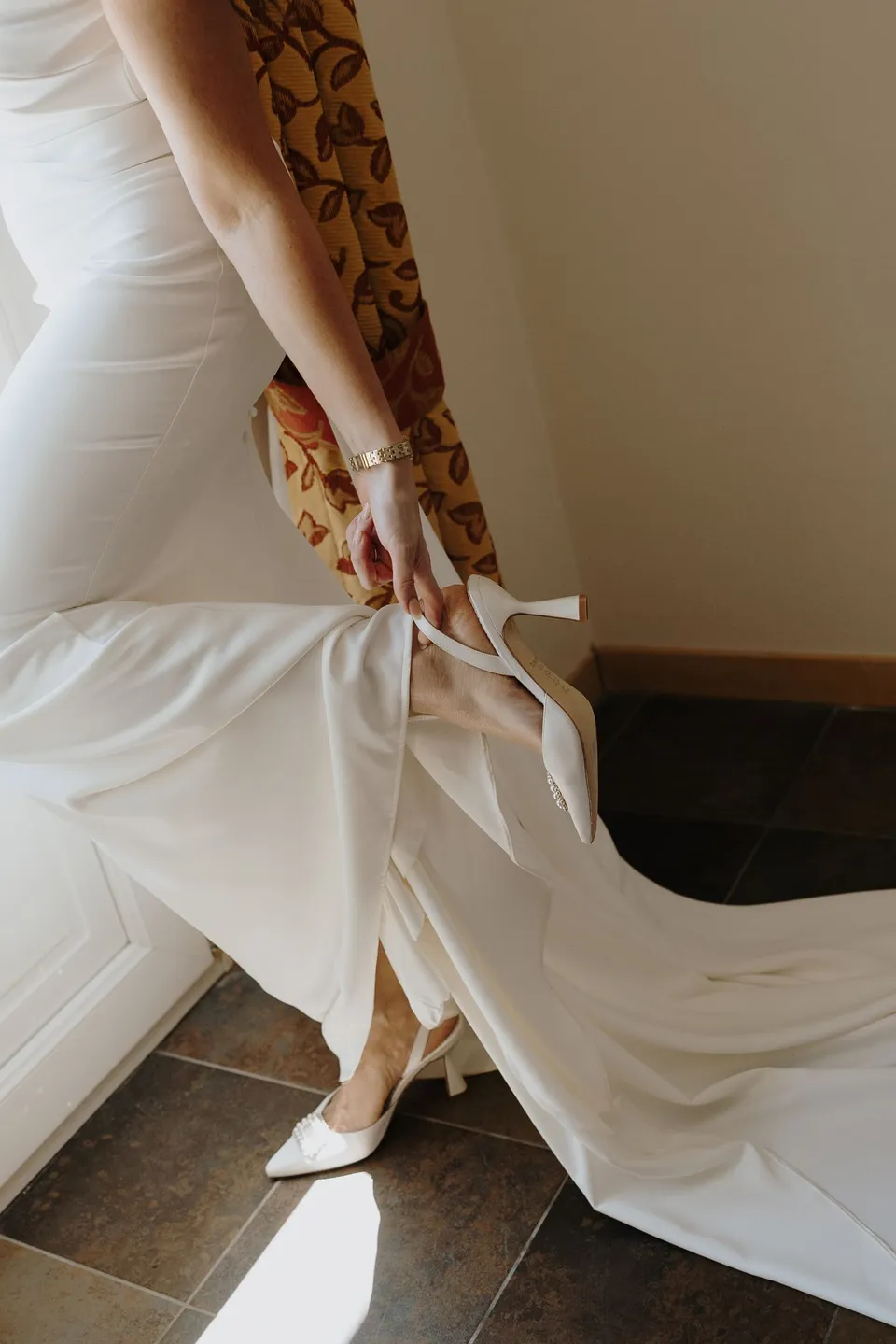 Close view of Lyndal lifting her white dress and train above a pointed heel beside the curtains at Hotel Villa Marie in Tremezzo, at Lake Como in Lombardy, Italy, for an Elopement Collective elopement. Photograph by George Bowden.