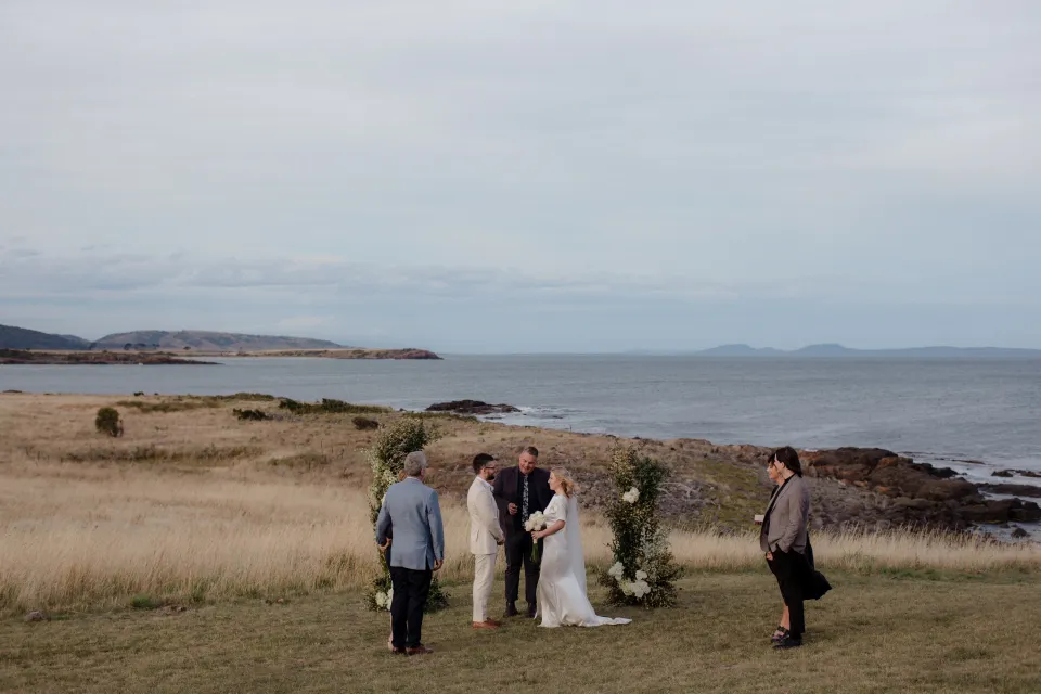 A wide view of the intimate ceremony on the lawn above Great Oyster Bay, at Thalia Haven on the East Coast of Tasmania, Australia, for an Elopement Collective elopement. Photograph by Joey Willis.