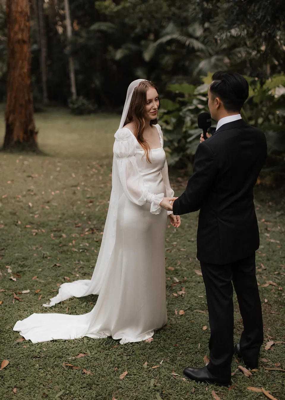 Elyse smiling at Jonathan while holding his hand during their vows. At Fig Tree Villa in Ewingsdale, Byron Bay, for an Elopement Collective elopement. Photograph by Bulb Creative.