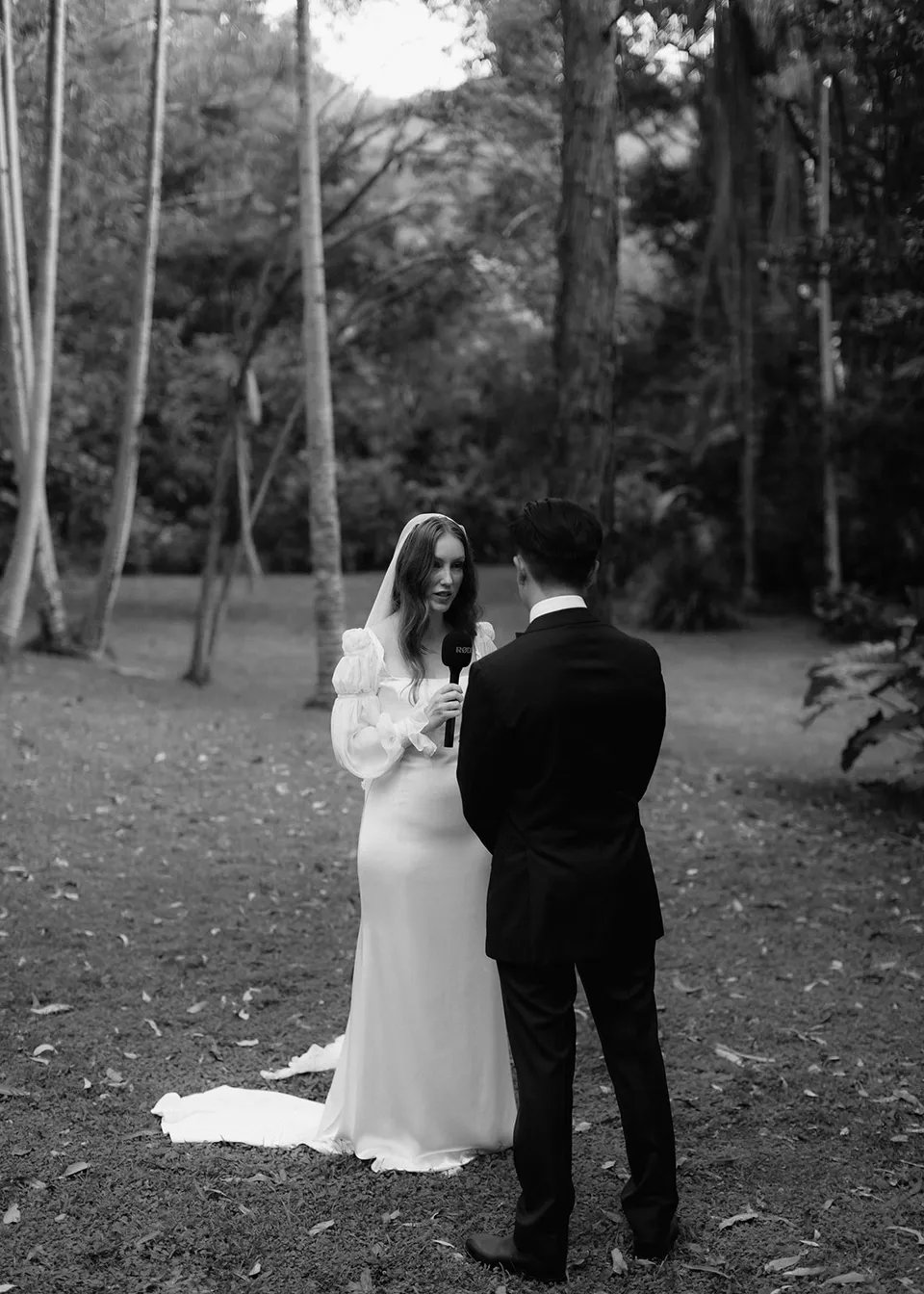 Black-and-white rear view of Jonathan listening to Elyse's vows. At Fig Tree Villa in Ewingsdale, Byron Bay, for an Elopement Collective elopement. Photograph by Bulb Creative.