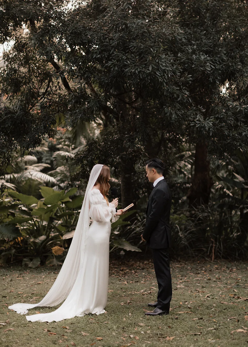 Elyse reading her personal vows beneath the trees. At Fig Tree Villa in Ewingsdale, Byron Bay, for an Elopement Collective elopement. Photograph by Bulb Creative.