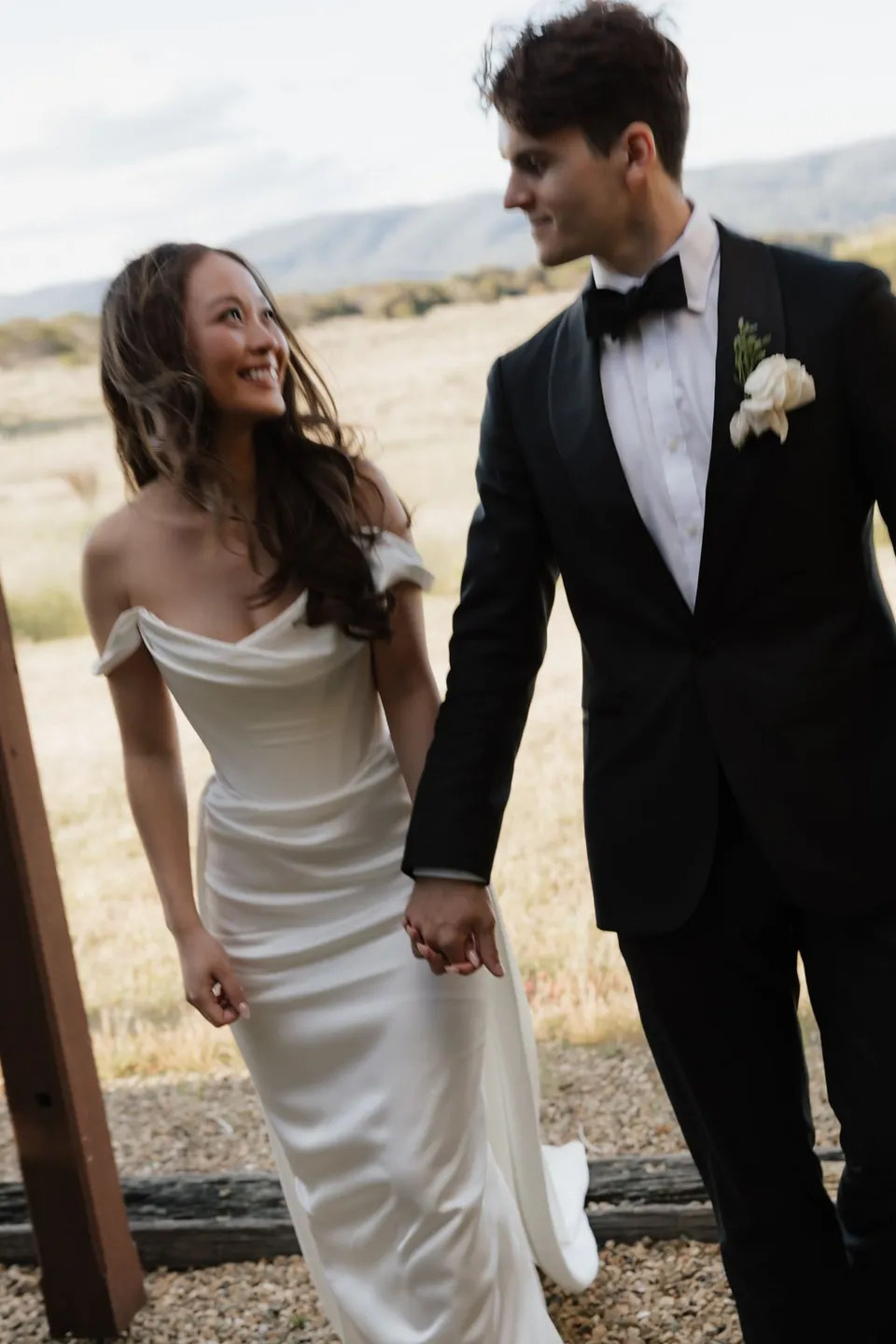 Clara and Harry smiling at each other as they walk hand in hand through the stone courtyard, at Thalia Haven on the East Coast of Tasmania, for an Elopement Collective elopement. Photograph by Bulb Creative.
