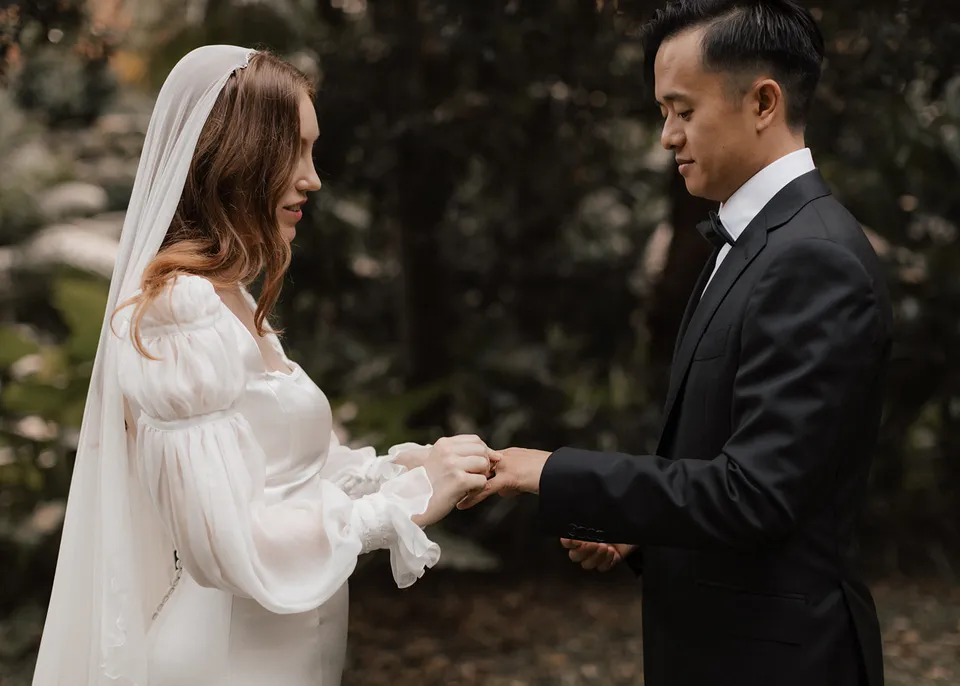 Elyse and Jonathan smiling as they exchange wedding rings. At Fig Tree Villa in Ewingsdale, Byron Bay, for an Elopement Collective elopement. Photograph by Bulb Creative.