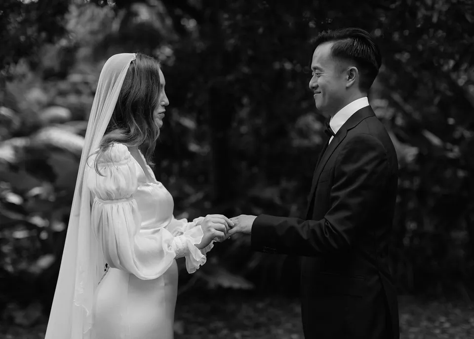 Black-and-white photograph of the couple laughing during their ring exchange. At Fig Tree Villa in Ewingsdale, Byron Bay, for an Elopement Collective elopement. Photograph by Bulb Creative.