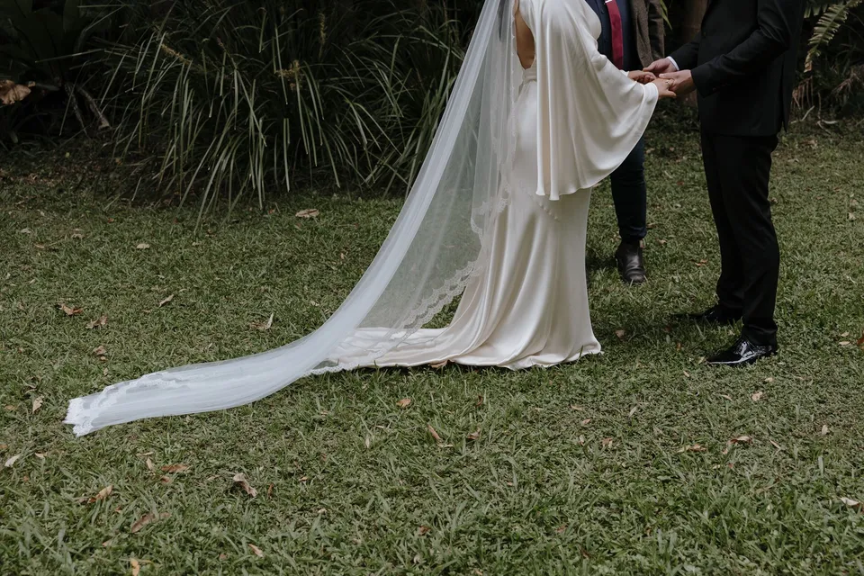 Detail of Laura's long veil and flowing sleeves as she holds Matthew's hands. At Fig Tree Villa in Ewingsdale, Byron Bay, for an Elopement Collective elopement. Photograph by George Bowden.
