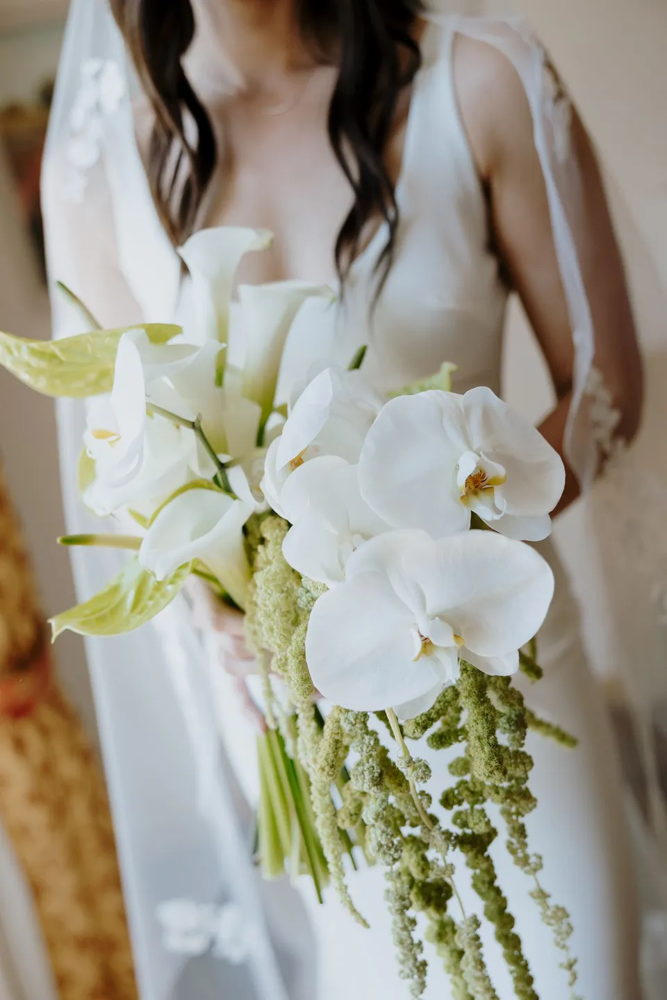 Lyndal holding a bouquet of white calla lilies, heart-shaped white blooms and trailing greenery by Garden of Love against her white dress, at Lake Como in Lombardy, Italy, for an Elopement Collective elopement. Photograph by George Bowden.