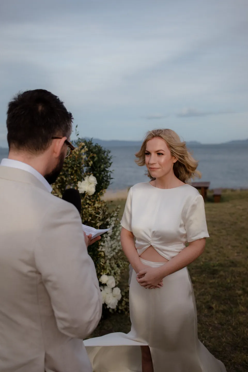 Jack reading from his vow cards while Jemmah smiles at him, at Thalia Haven on the East Coast of Tasmania, Australia, for an Elopement Collective elopement. Photograph by Joey Willis.