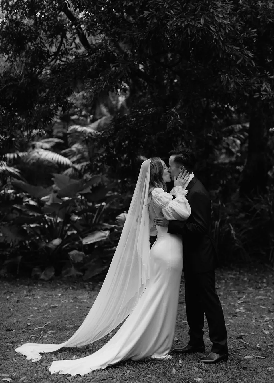Black-and-white wide view of the couple kissing after their vows. At Fig Tree Villa in Ewingsdale, Byron Bay, for an Elopement Collective elopement. Photograph by Bulb Creative.
