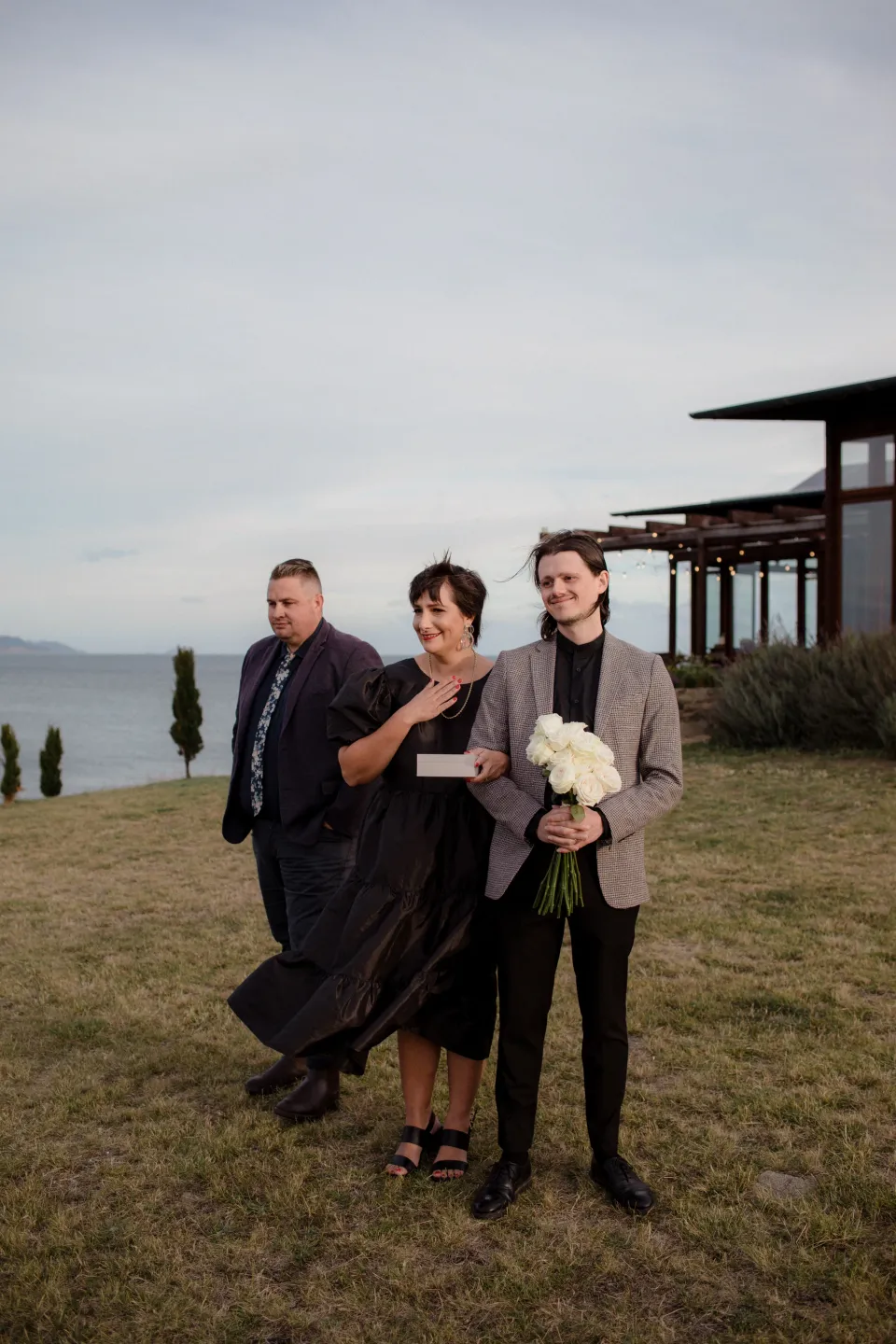 Loved ones watching the ceremony with the stone house behind them, at Thalia Haven on the East Coast of Tasmania, Australia, for an Elopement Collective elopement. Photograph by Joey Willis.
