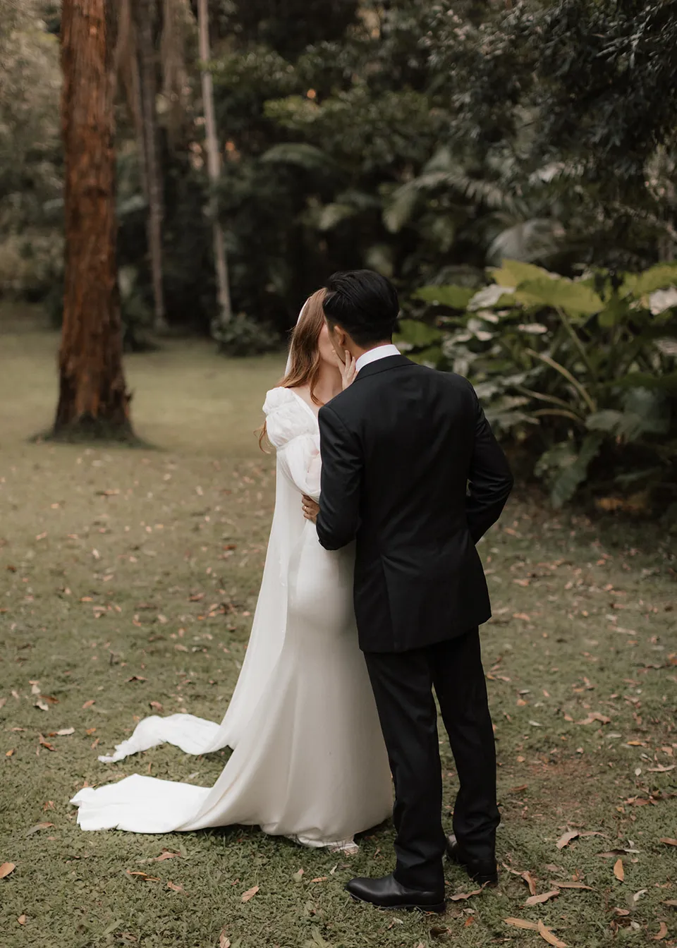 Rear view of Elyse and Jonathan kissing in the garden. At Fig Tree Villa in Ewingsdale, Byron Bay, for an Elopement Collective elopement. Photograph by Bulb Creative.