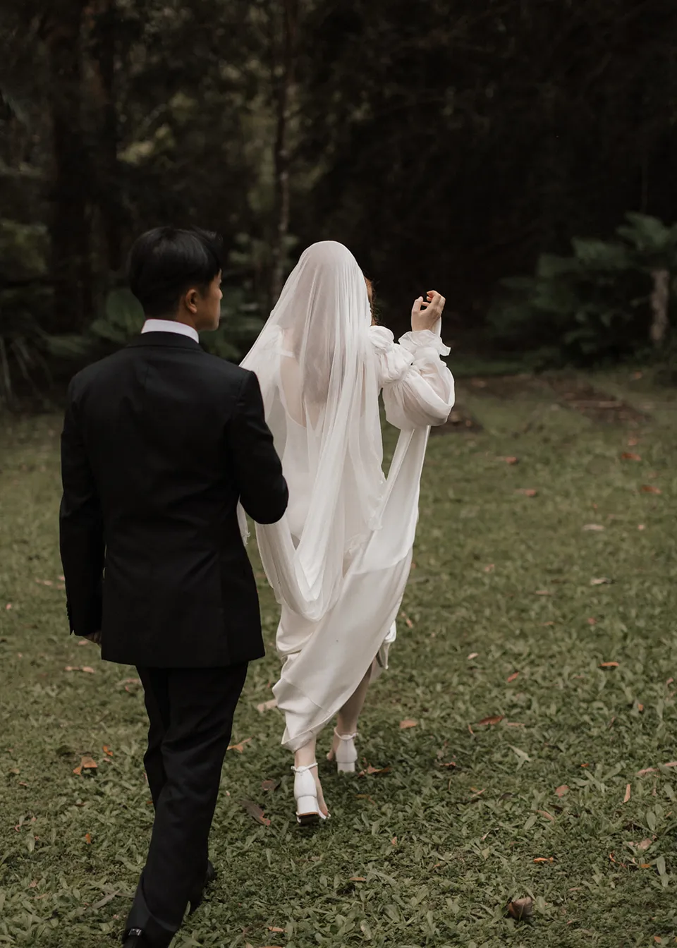 Jonathan following Elyse across the lawn as she lifts her dress. At Fig Tree Villa in Ewingsdale, Byron Bay, for an Elopement Collective elopement. Photograph by Bulb Creative.