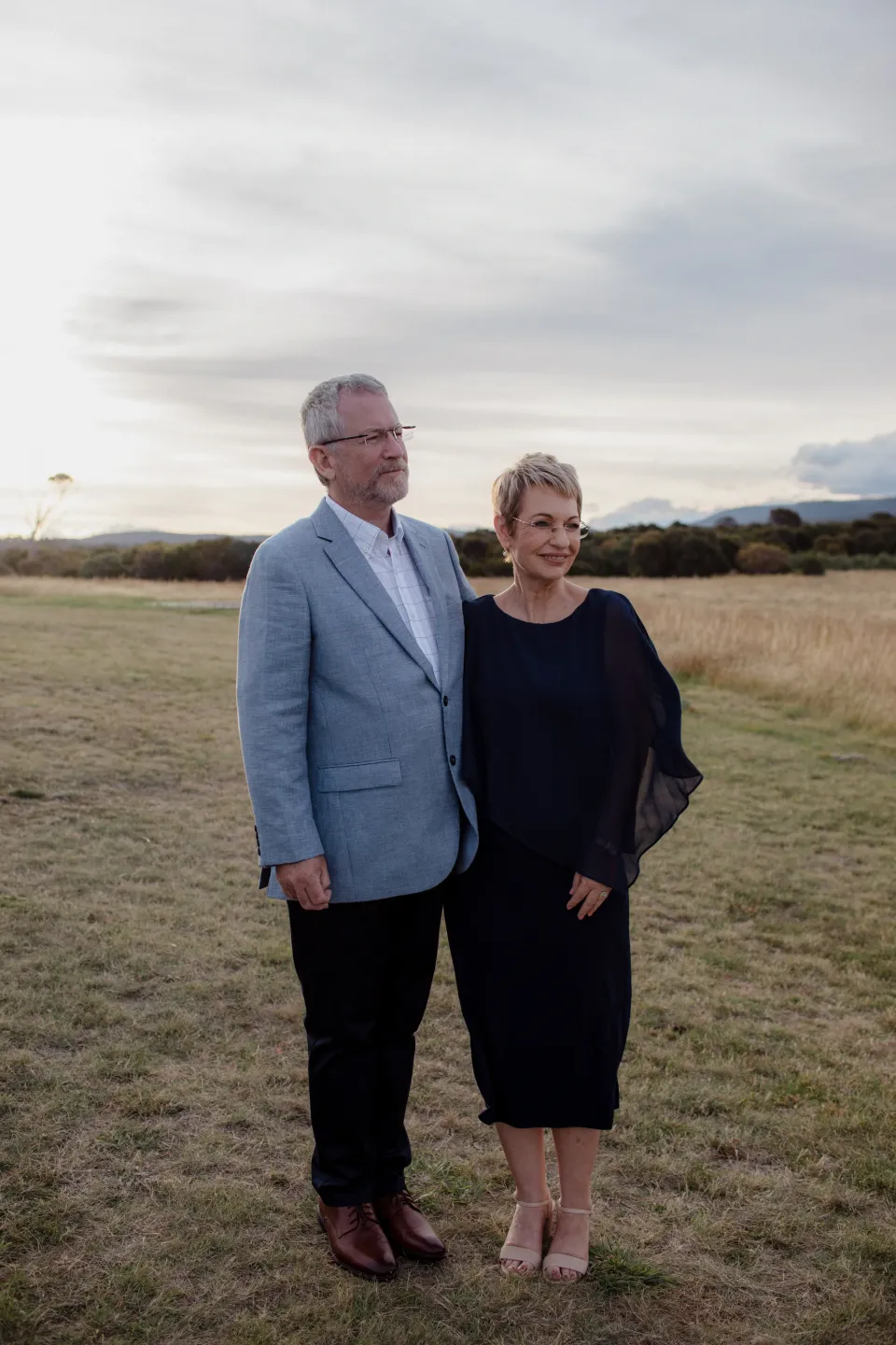 Two loved ones watching the ceremony beneath a cloudy sky, at Thalia Haven on the East Coast of Tasmania, Australia, for an Elopement Collective elopement. Photograph by Joey Willis.