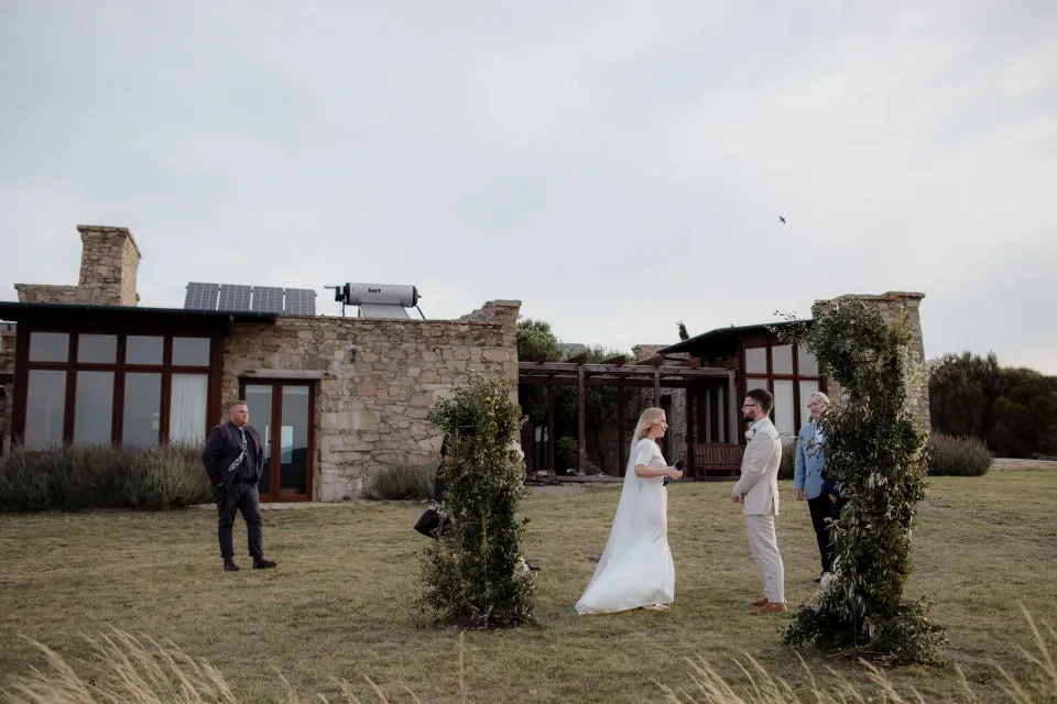 A wide view of Jemmah and Jack’s ceremony between flowers by The Romantics, at Thalia Haven on the East Coast of Tasmania, Australia, for an Elopement Collective elopement. Photograph by Joey Willis.