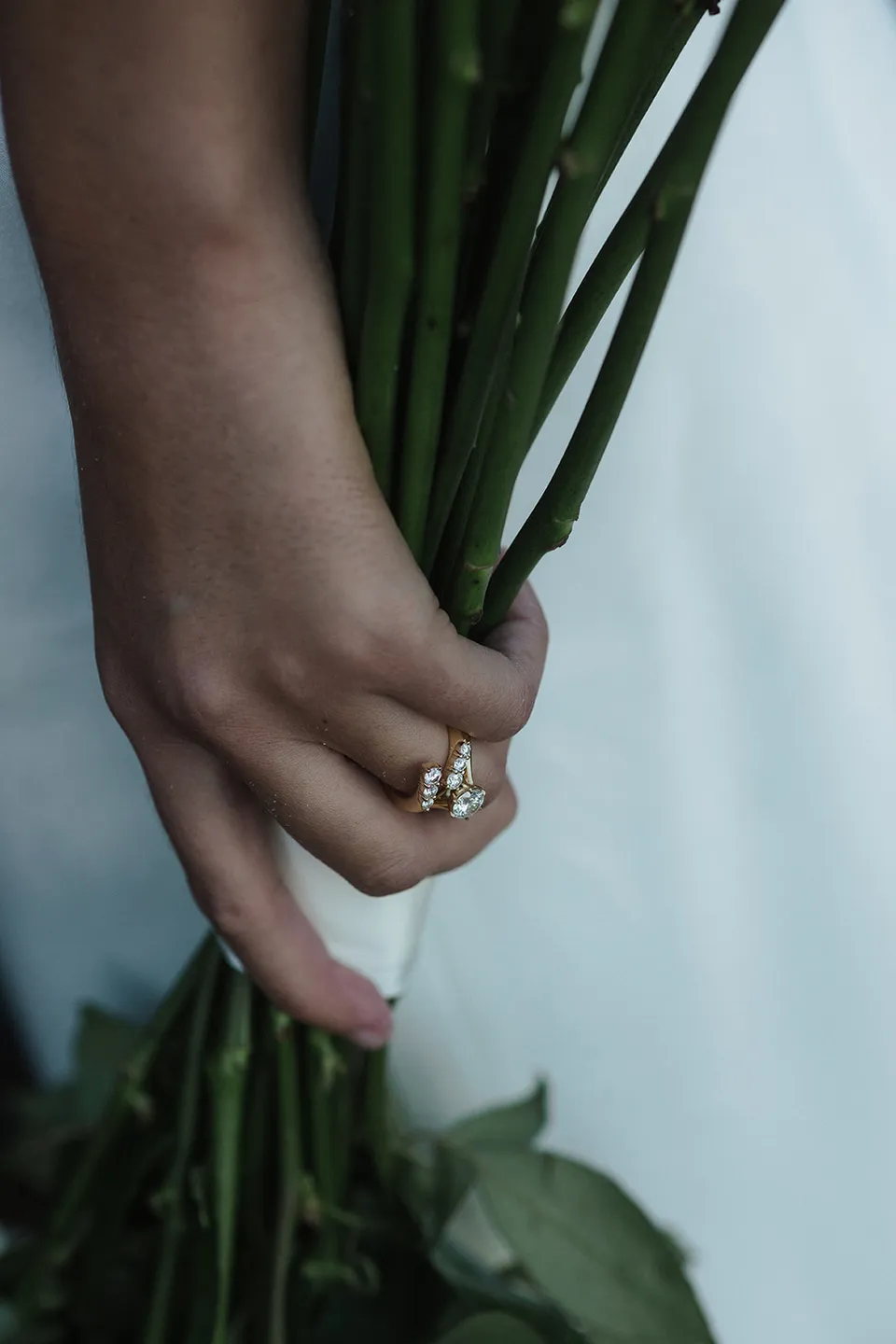 Close-up of Rachel's wedding ring and hand holding the stems of her bouquet, with flowers by Fifth Avenue Florist. At Whites Beach, Broken Head, near Byron Bay, for an Elopement Collective elopement. Photograph by Jason Lucas.