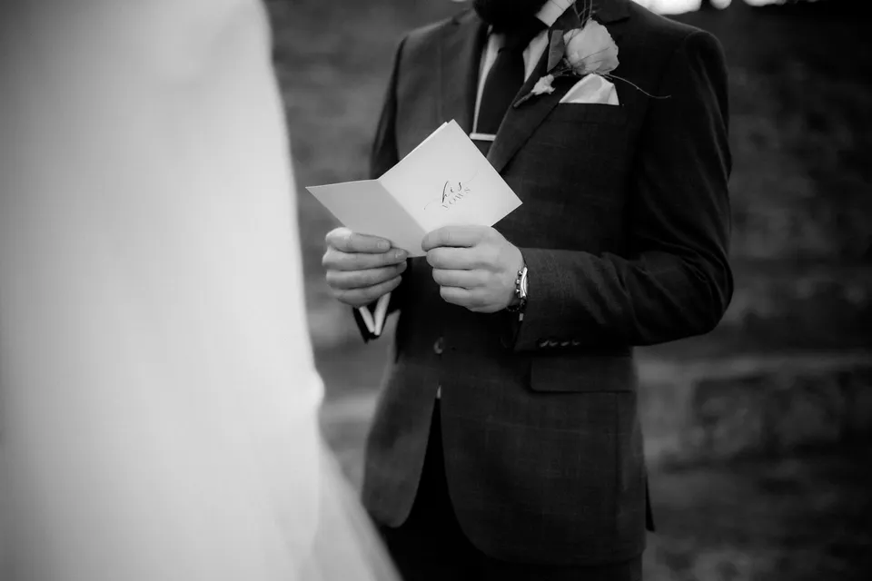 Black and white detail of Russell holding his vow booklet, with his floral buttonhole by The Romantics. At Piermont Retreat on Tasmania’s east coast, for an Elopement Collective elopement. Photograph by Omar of By The Wilde.
