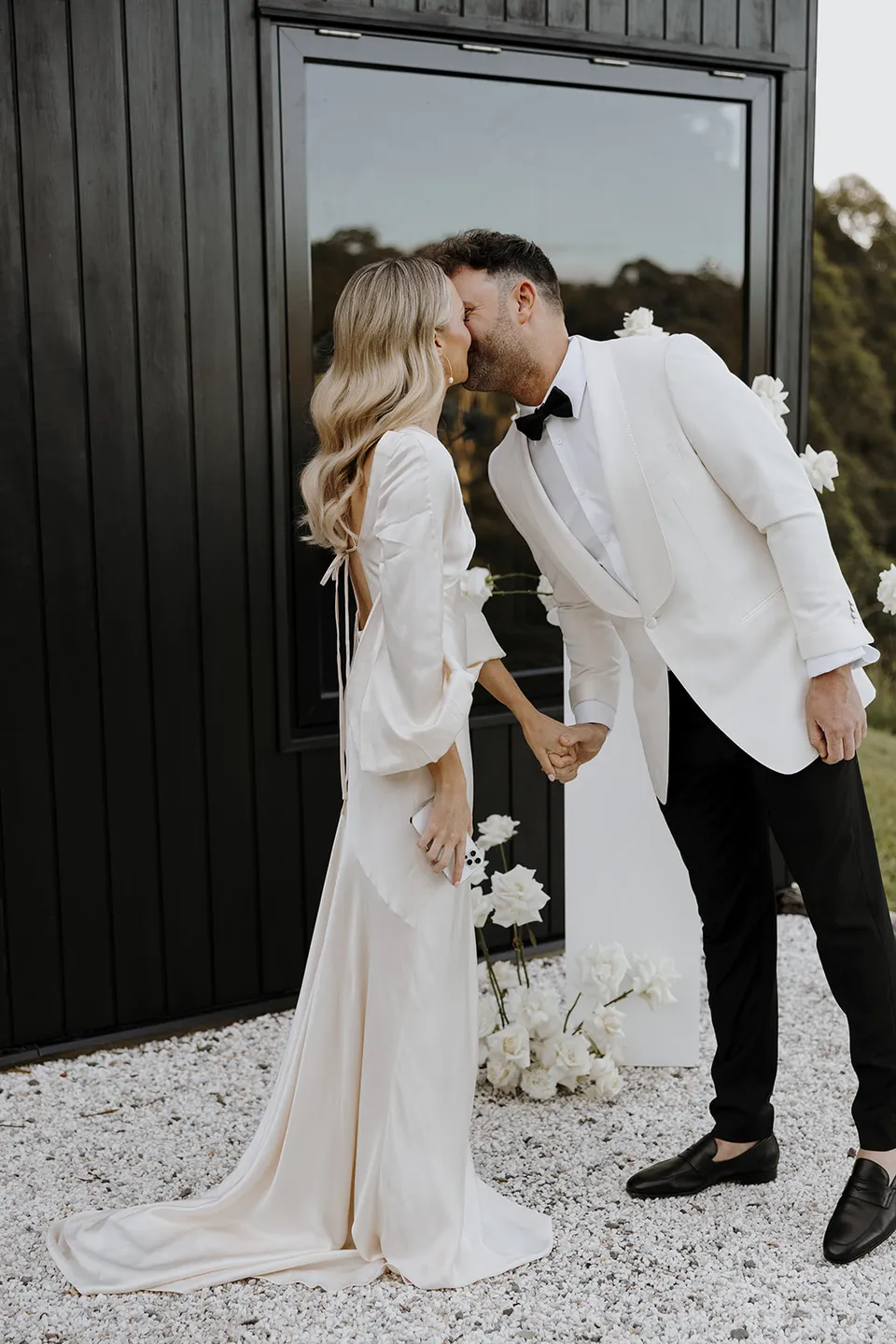 Gabrielle and Greg kissing beside the white ceremony flowers and cabin window at Roundhill Retreat in Obi Obi, Sunshine Coast Hinterland, for their Elopement Collective elopement.