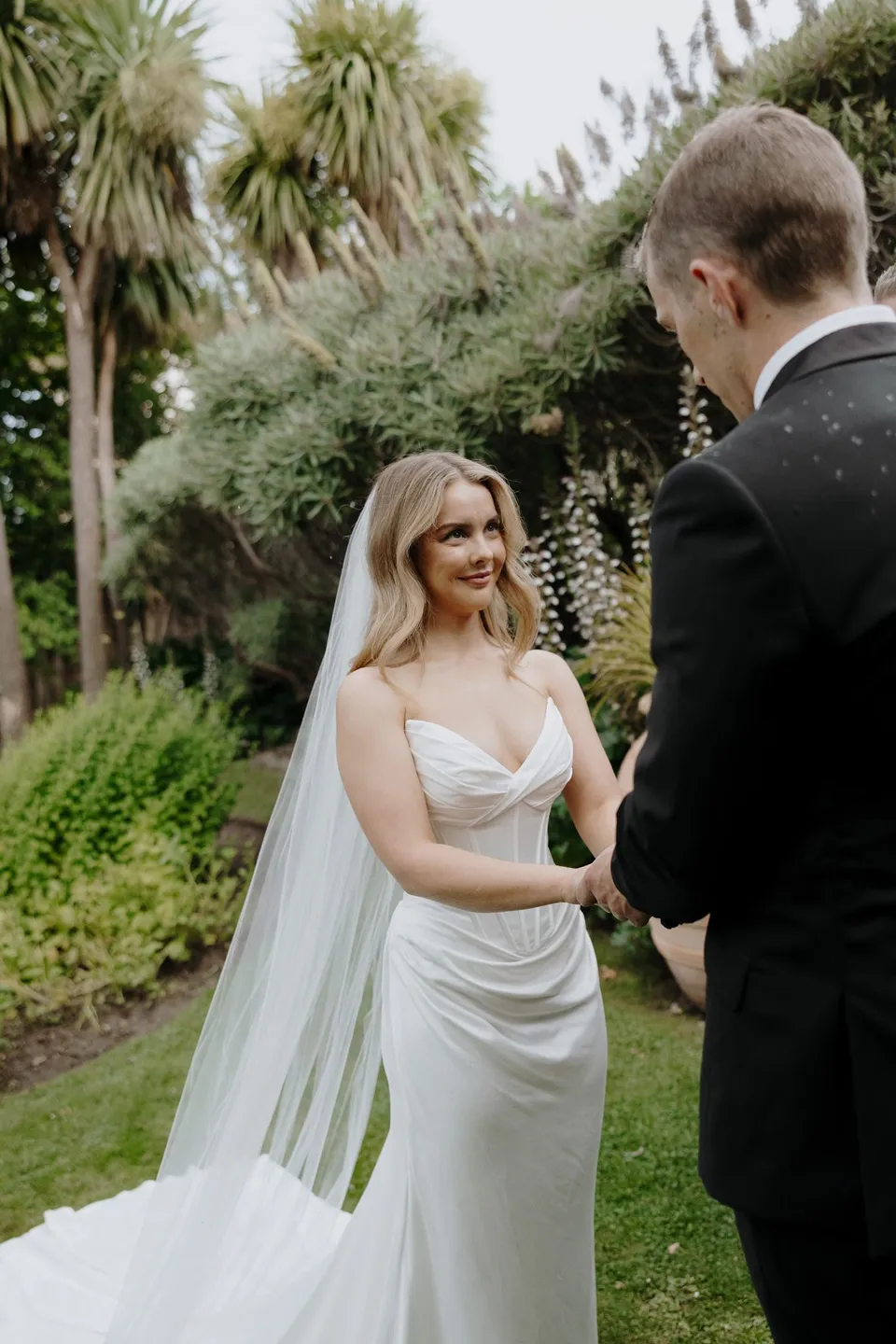 Tanesha smiling at Andrew as they hold hands in the garden during their ceremony, at Islington Hotel in South Hobart, Tasmania, Australia, for an Elopement Collective summer elopement. Photograph by George Bowden.