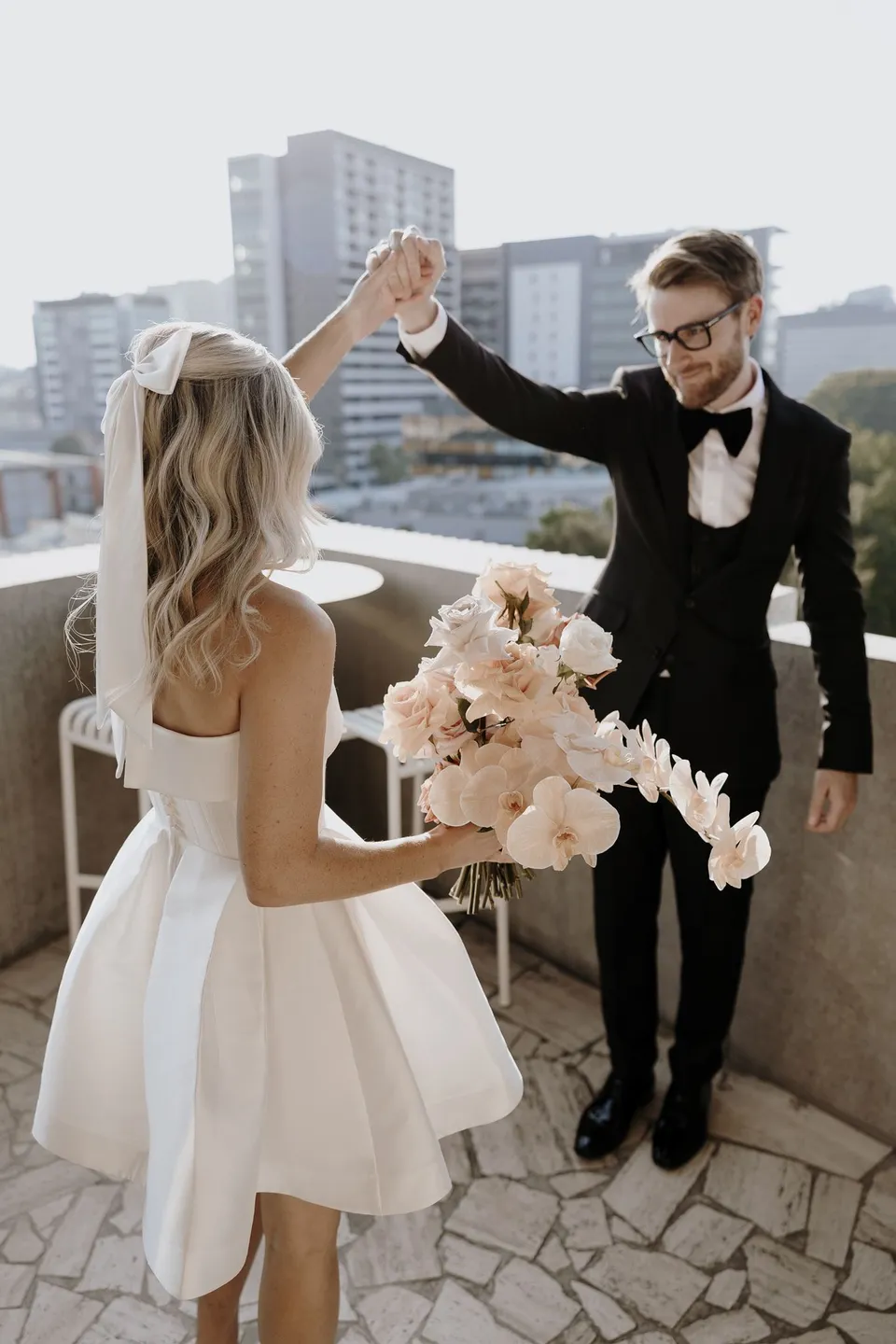 Adam lifting Danielle’s hand as she turns beside him on the terrace, carrying her bouquet, during Danielle and Adam’s Elopement Collective elopement at The Calile Hotel in Fortitude Valley, Brisbane.