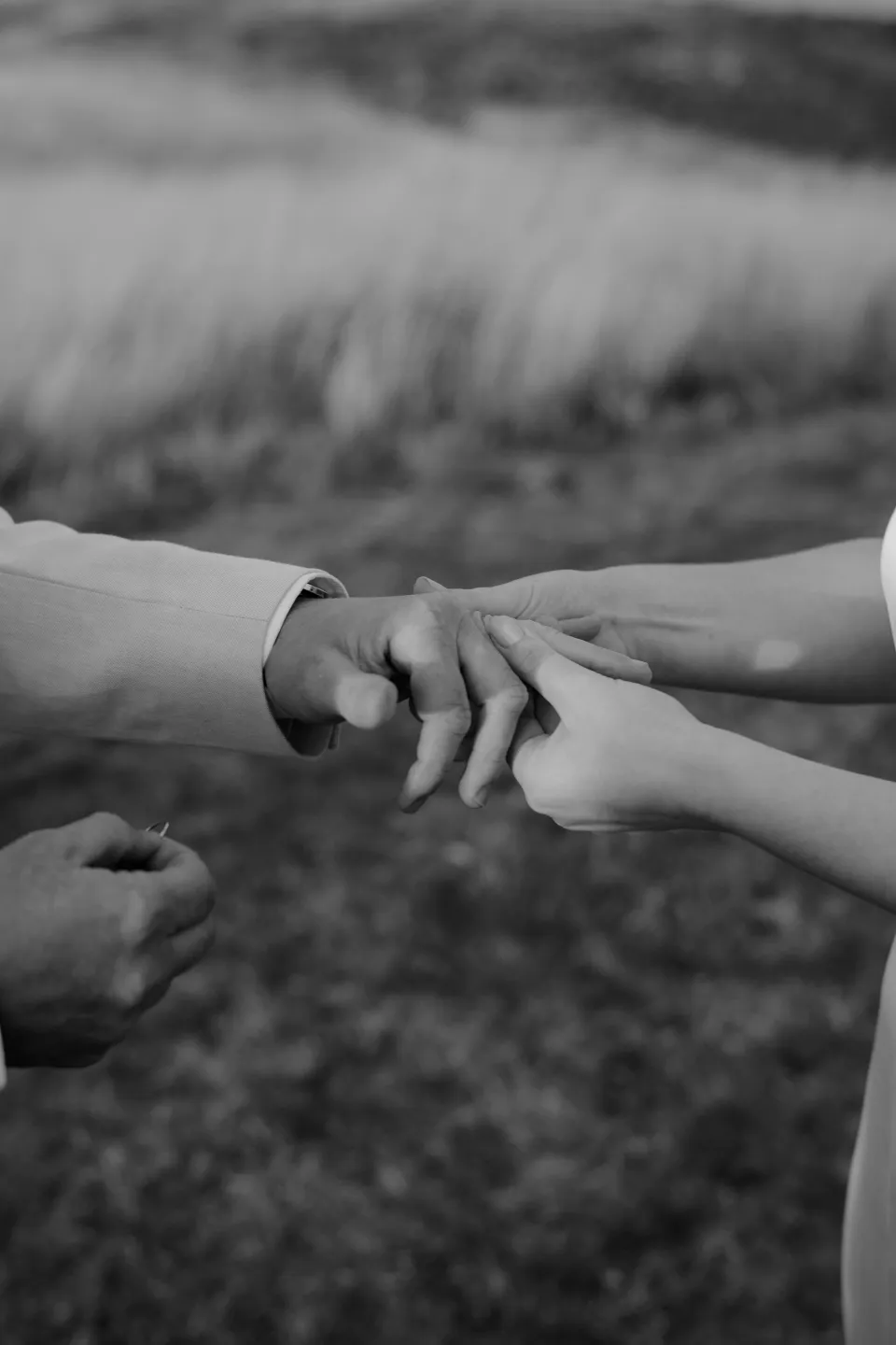 Black and white close-up of a wedding ring being placed on a finger, at Thalia Haven on the East Coast of Tasmania, Australia, for an Elopement Collective elopement. Photograph by Joey Willis.