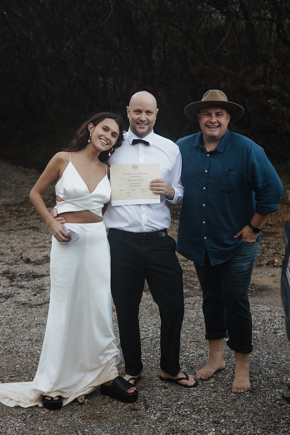 Rachel and Dane smiling for a relaxed photograph with celebrant Josh Withers beside the beach. At Whites Beach, Broken Head, near Byron Bay, for an Elopement Collective elopement. Photograph by Jason Lucas.