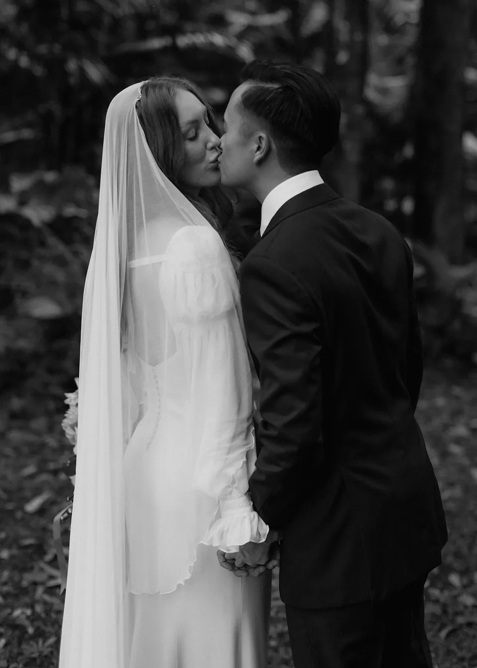 Black-and-white close portrait of Jonathan kissing Elyse's cheek. At Fig Tree Villa in Ewingsdale, Byron Bay, for an Elopement Collective elopement. Photograph by Bulb Creative.