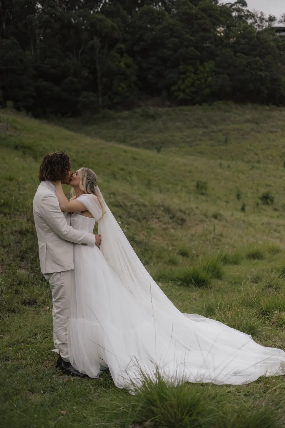 Bridget and James embracing in a grassy paddock after their ceremony. At Cudgera Creek in northern New South Wales, for an Elopement Collective elopement. Photograph by Bulb Creative.