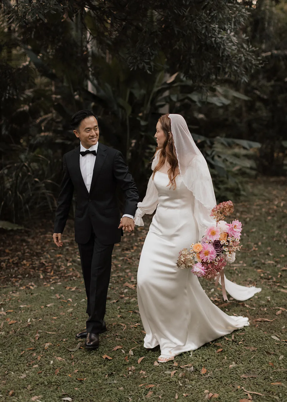 Elyse and Jonathan laughing as they walk together with her bouquet, with flowers by The Perfect Party Co. At Fig Tree Villa in Ewingsdale, Byron Bay, for an Elopement Collective elopement. Photograph by Bulb Creative.