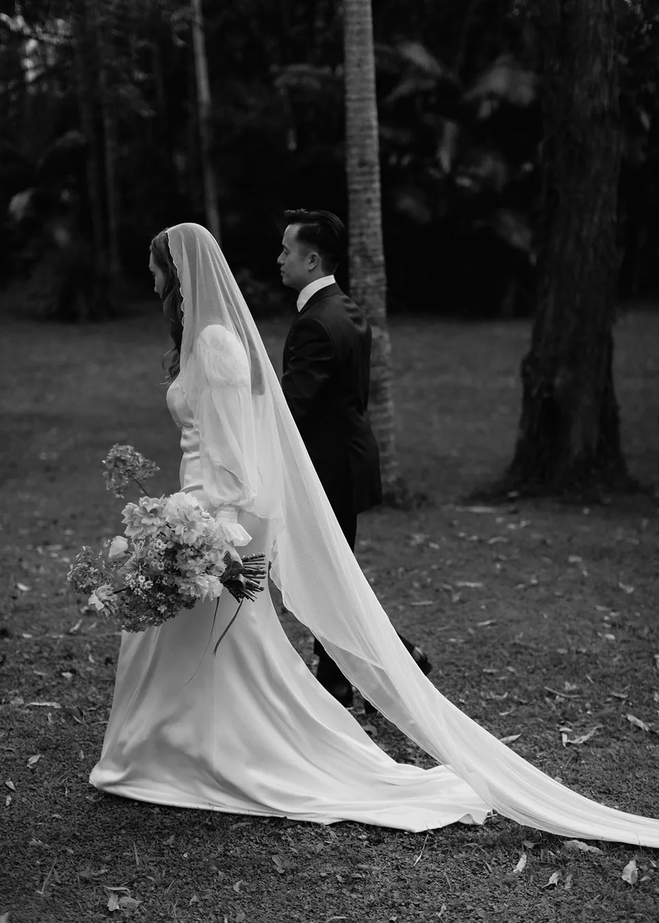 Black-and-white portrait of Elyse turning towards Jonathan, her veil sweeping behind her. At Fig Tree Villa in Ewingsdale, Byron Bay, for an Elopement Collective elopement. Photograph by Bulb Creative.