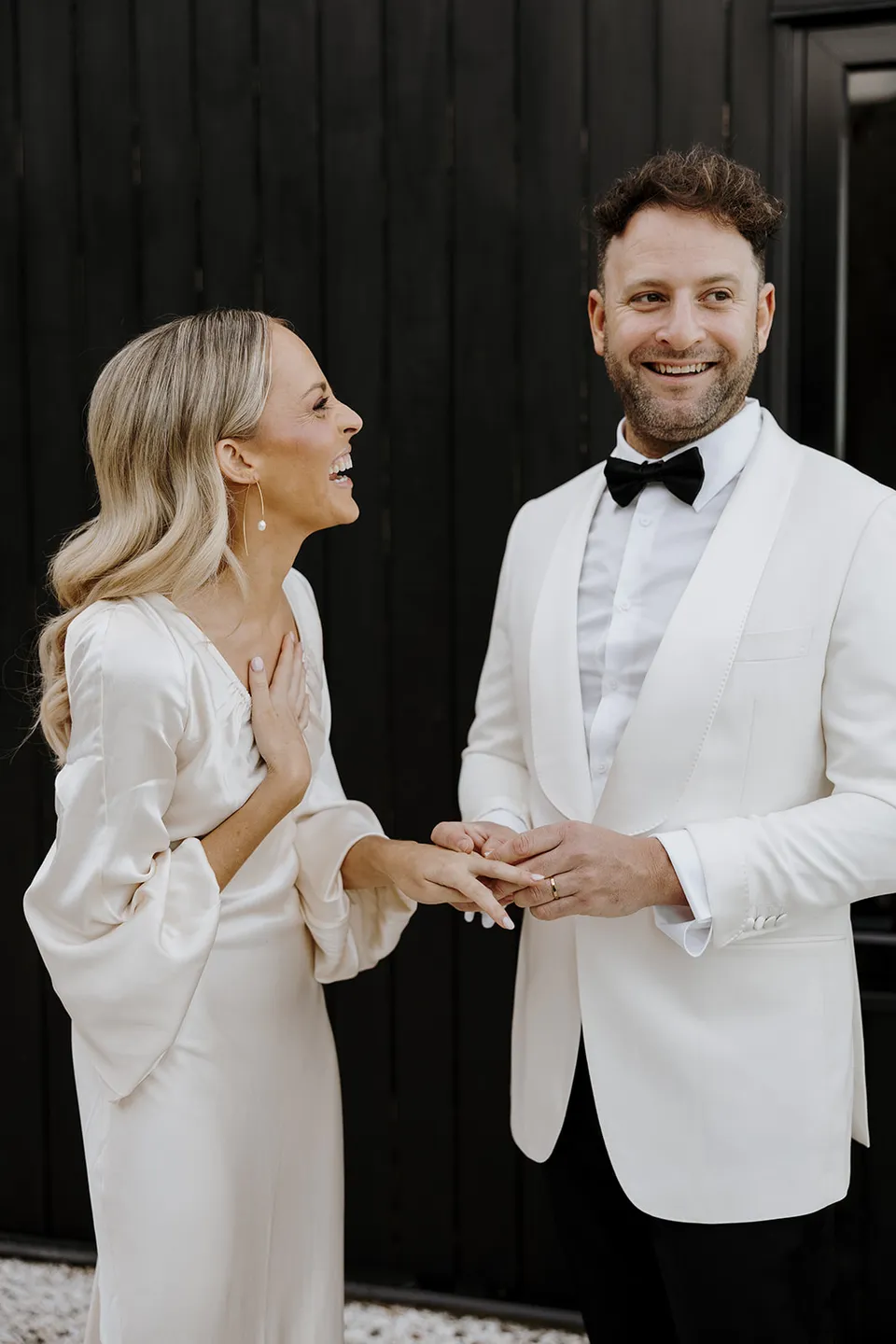 Greg smiling as Gabrielle looks towards him during their ring exchange beside the dark cabin at Roundhill Retreat in Obi Obi, Sunshine Coast Hinterland, for their Elopement Collective elopement.