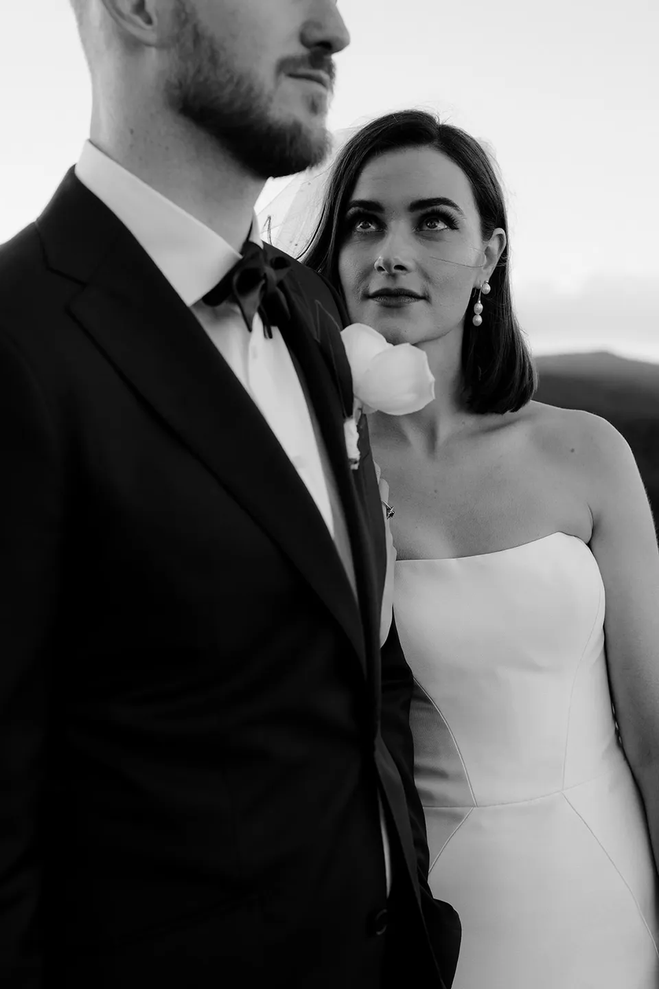 Black and white close portrait of Meg looking up at Ryan, with a white rose on his lapel. At The Keep on Tasmania’s east coast, for an Elopement Collective elopement. Photograph by Jenna Agius.