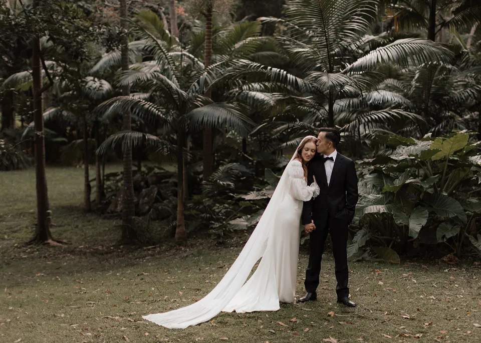 Wide portrait of the couple nestled among tree ferns and palms. At Fig Tree Villa in Ewingsdale, Byron Bay, for an Elopement Collective elopement. Photograph by Bulb Creative.