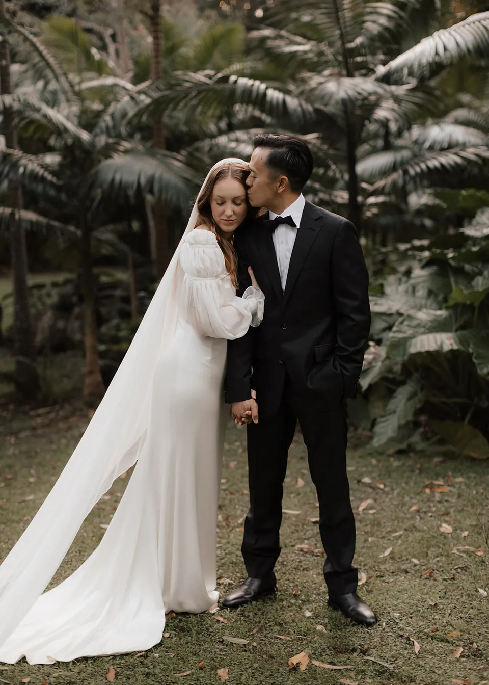 Elyse and Jonathan standing close beneath the tree ferns. At Fig Tree Villa in Ewingsdale, Byron Bay, for an Elopement Collective elopement. Photograph by Bulb Creative.