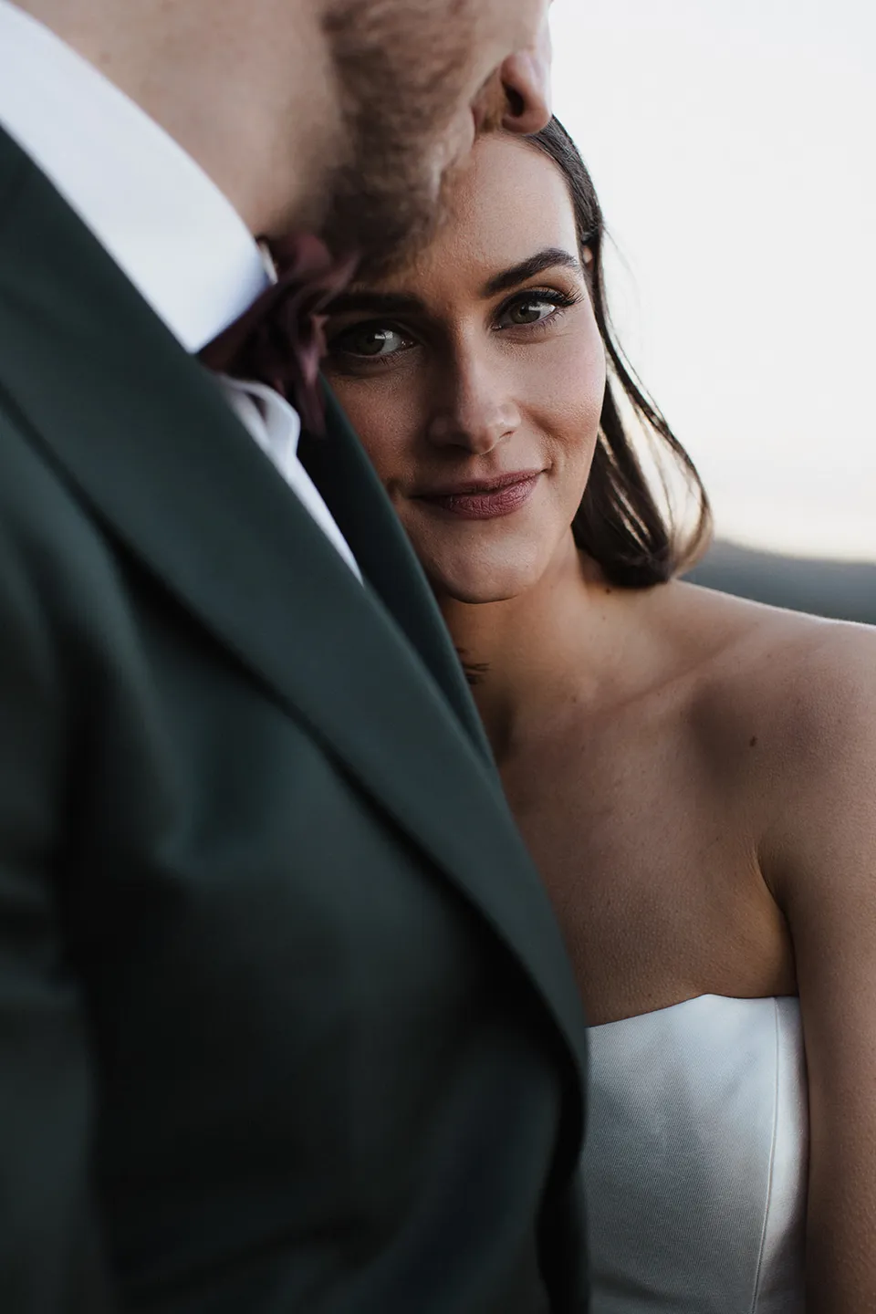 Close portrait of Meg leaning against Ryan’s dark green suit. At The Keep on Tasmania’s east coast, for an Elopement Collective elopement. Photograph by Jenna Agius.